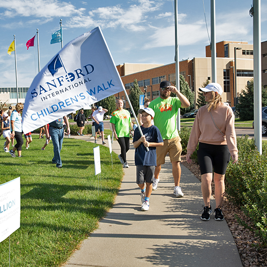 People walking on a sidewalk holding a Sanford flag